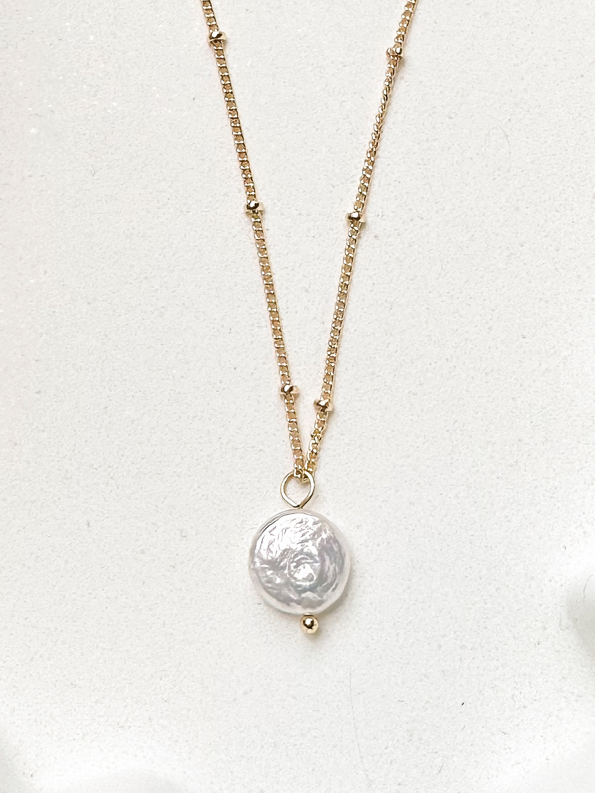 Freshwater pearl coin necklace with gold chain set against white background