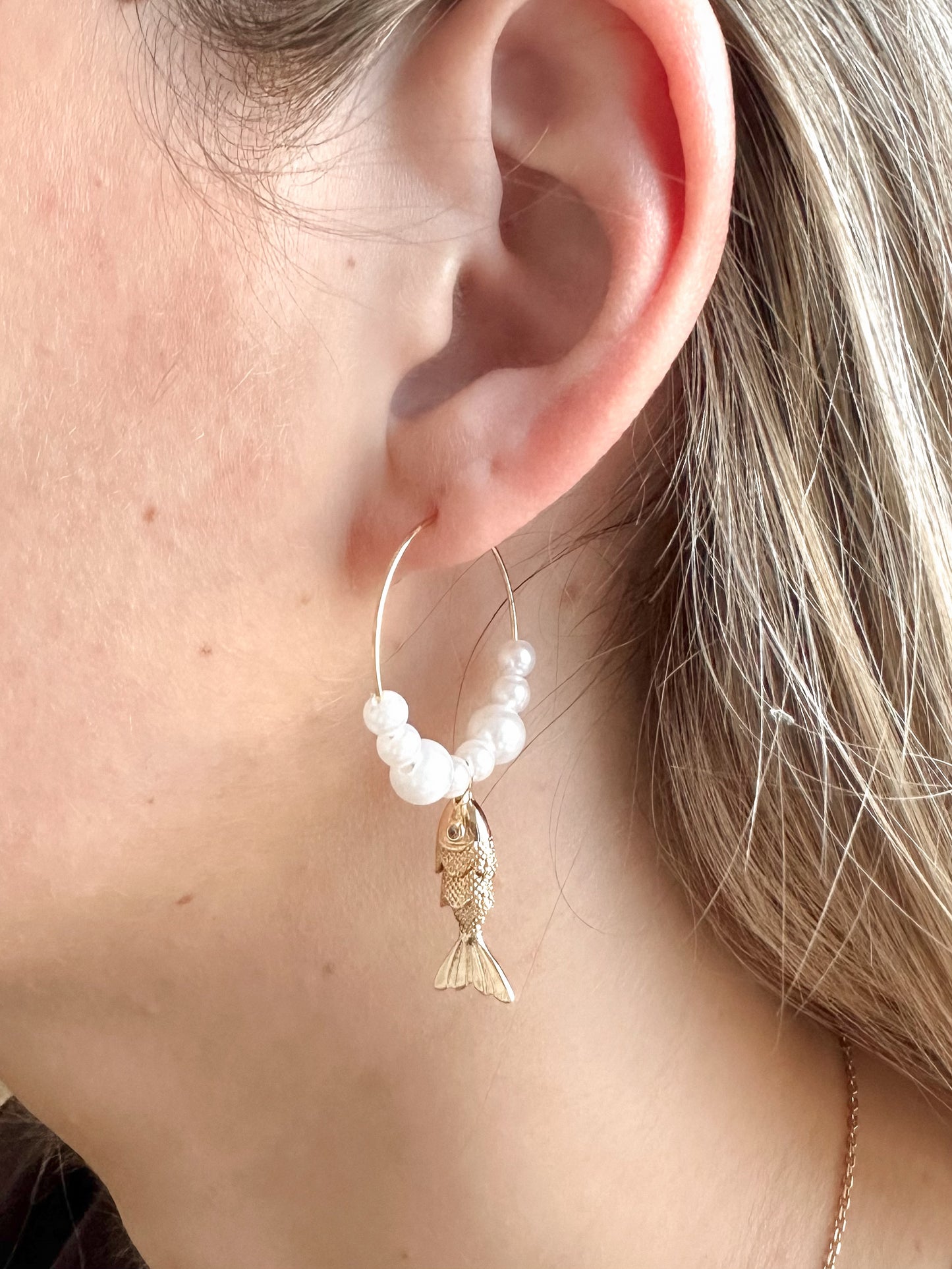 Earring with pearl beads and gold fish charm worn by a person