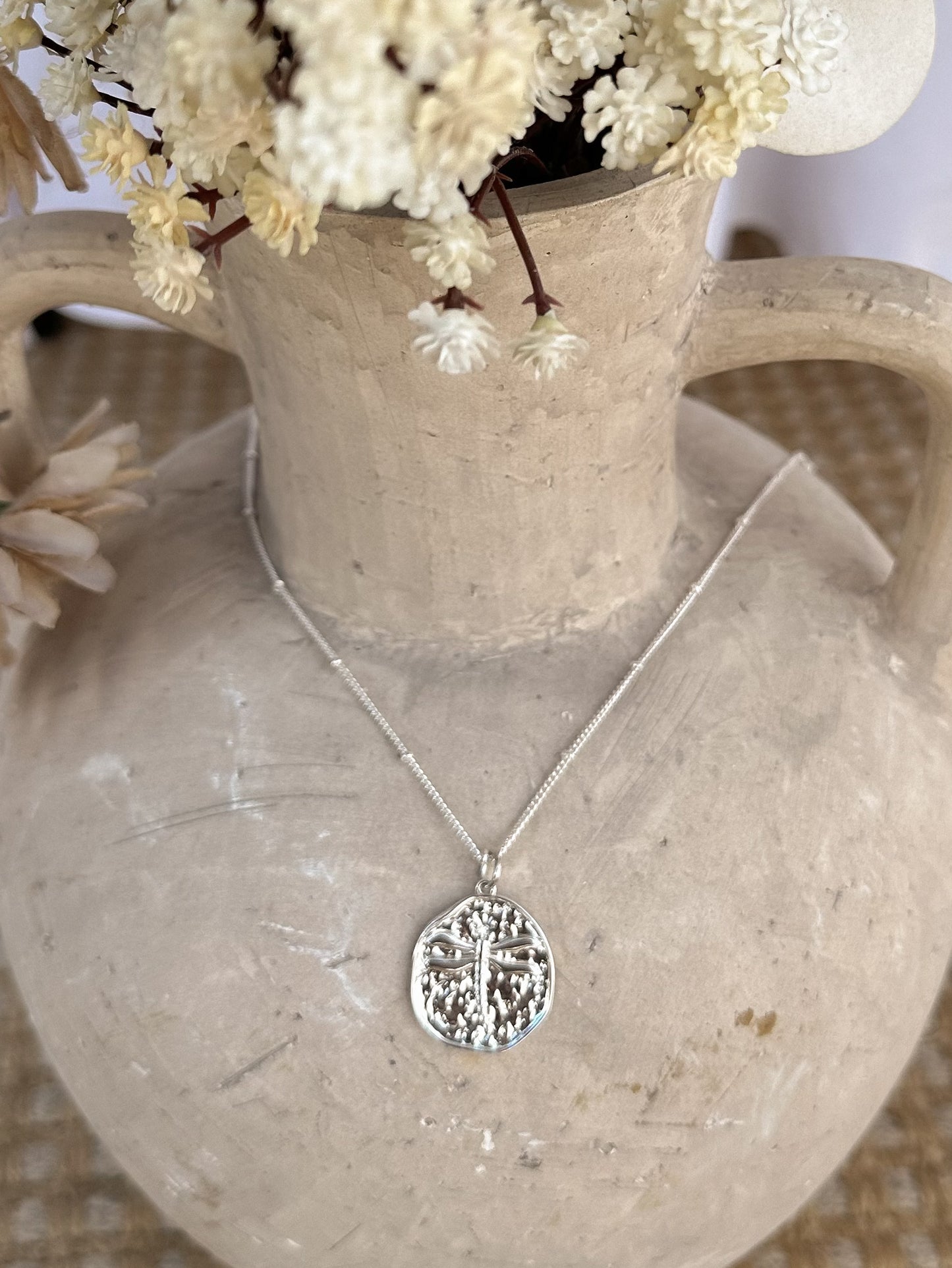 Silver dragonfly necklace on a stone vase with dried florals