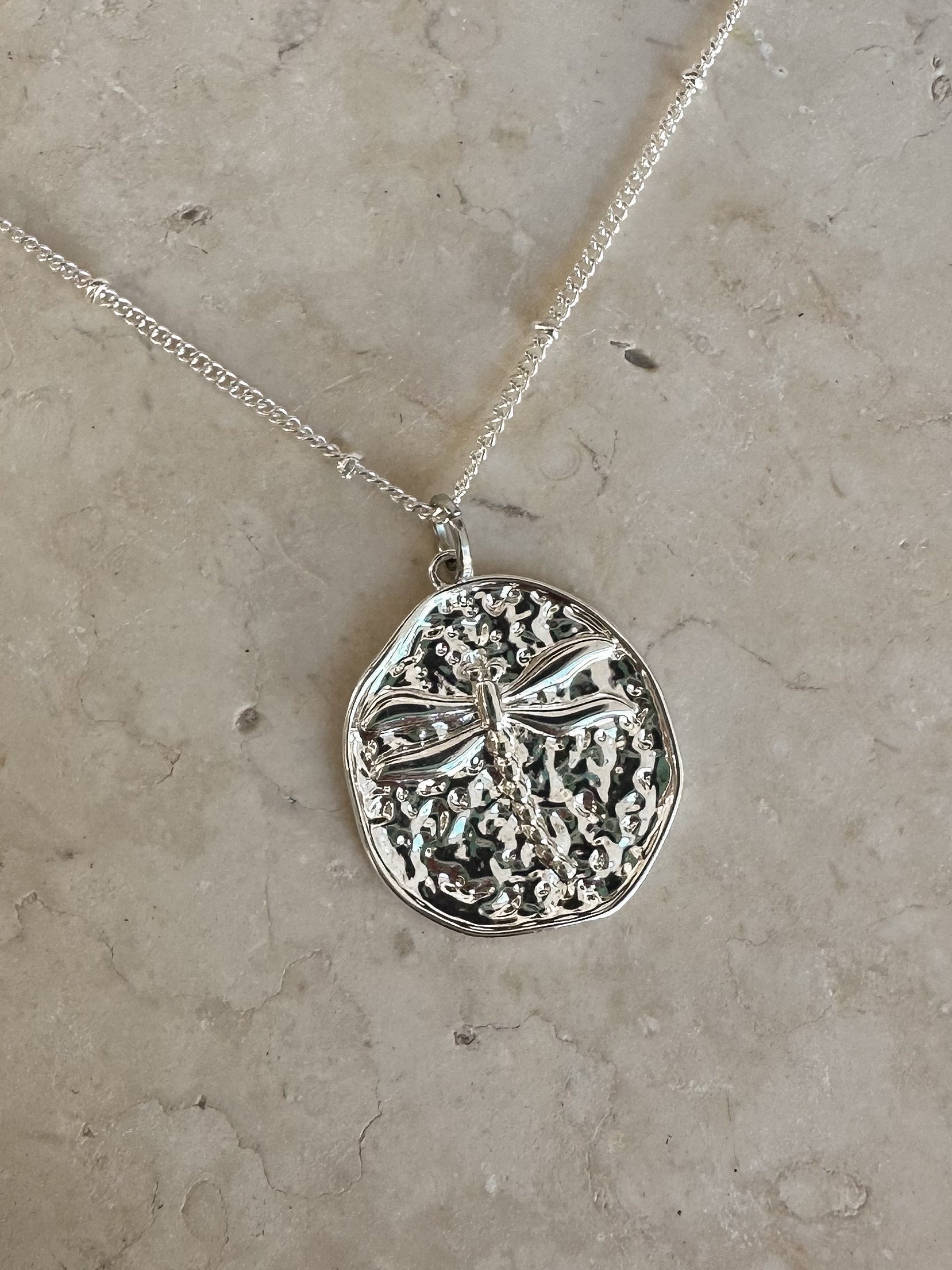Silver dragonfly pendant on a silver plated necklace chain on a stone background