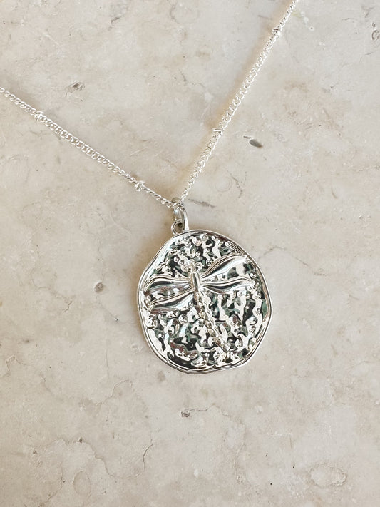 Silver dragonfly pendant on a silver plated necklace chain on a stone background