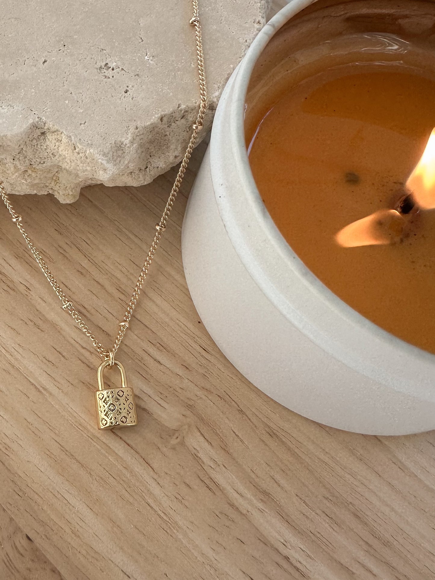 Gold patterned padlock pendant on a gold chain, on a travertine stone with a lit candle