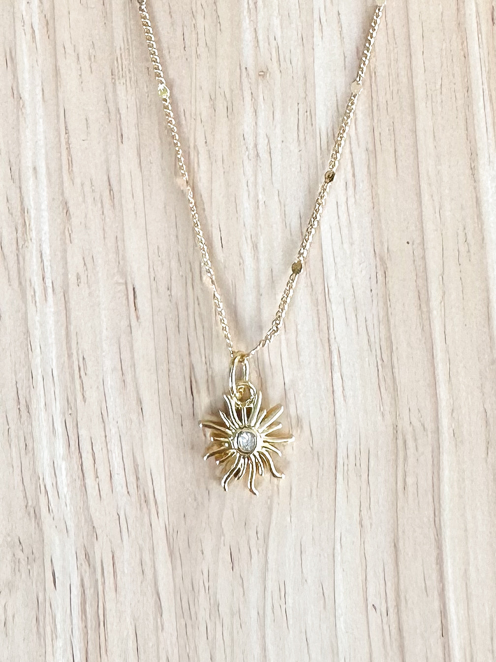 Sun pendant with cz centre on a gold plated chain on a timber background