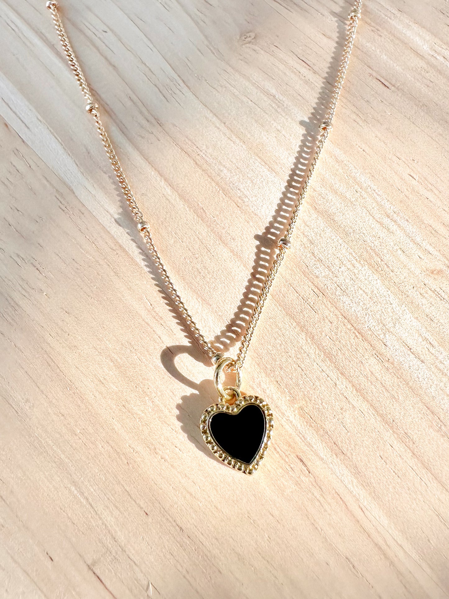 Black enamel heart pendant on a gold plated stainless steel chain on a timber background 