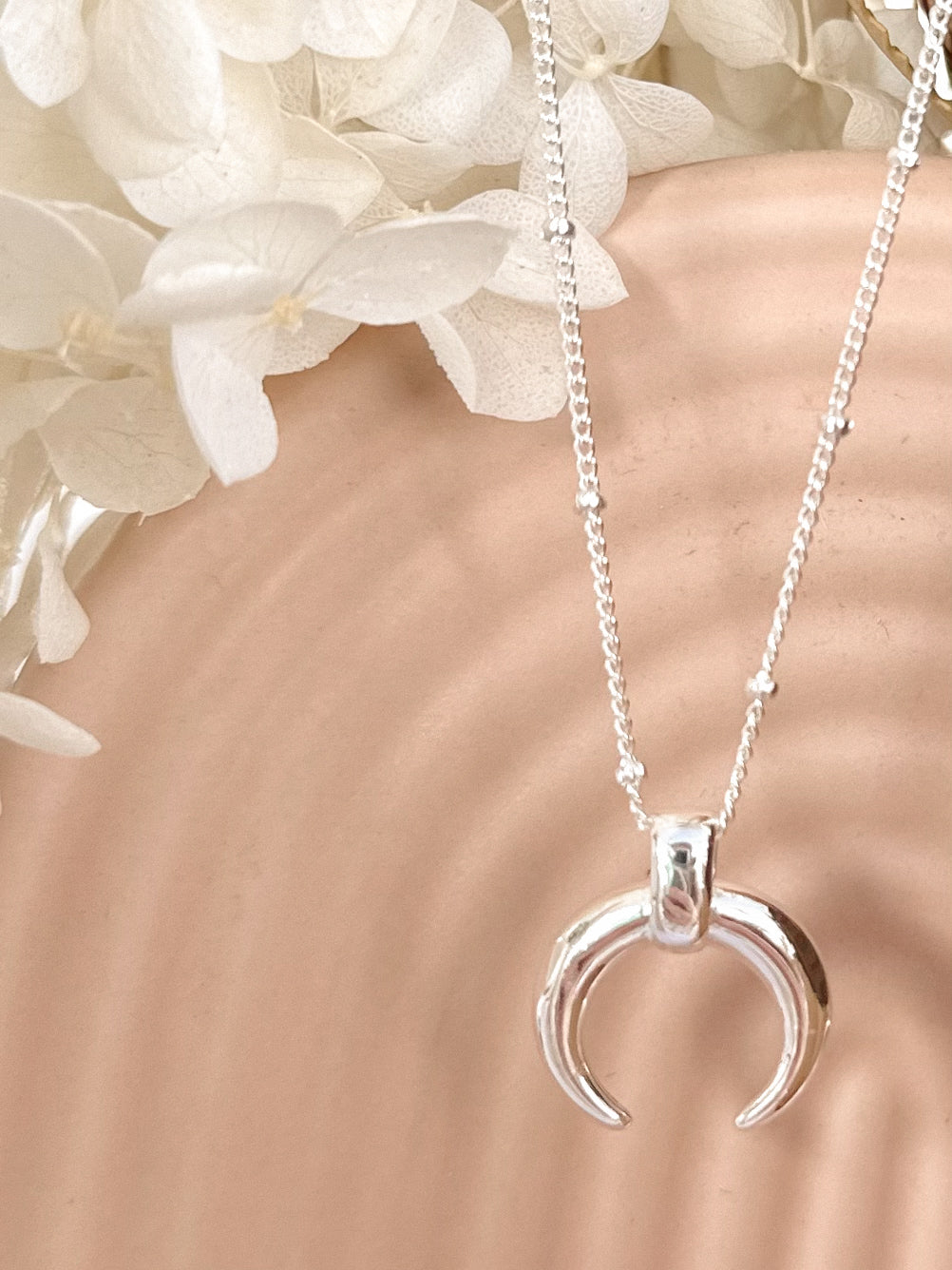 Silver crescent moon necklace draped on a arches vase with dried flowers