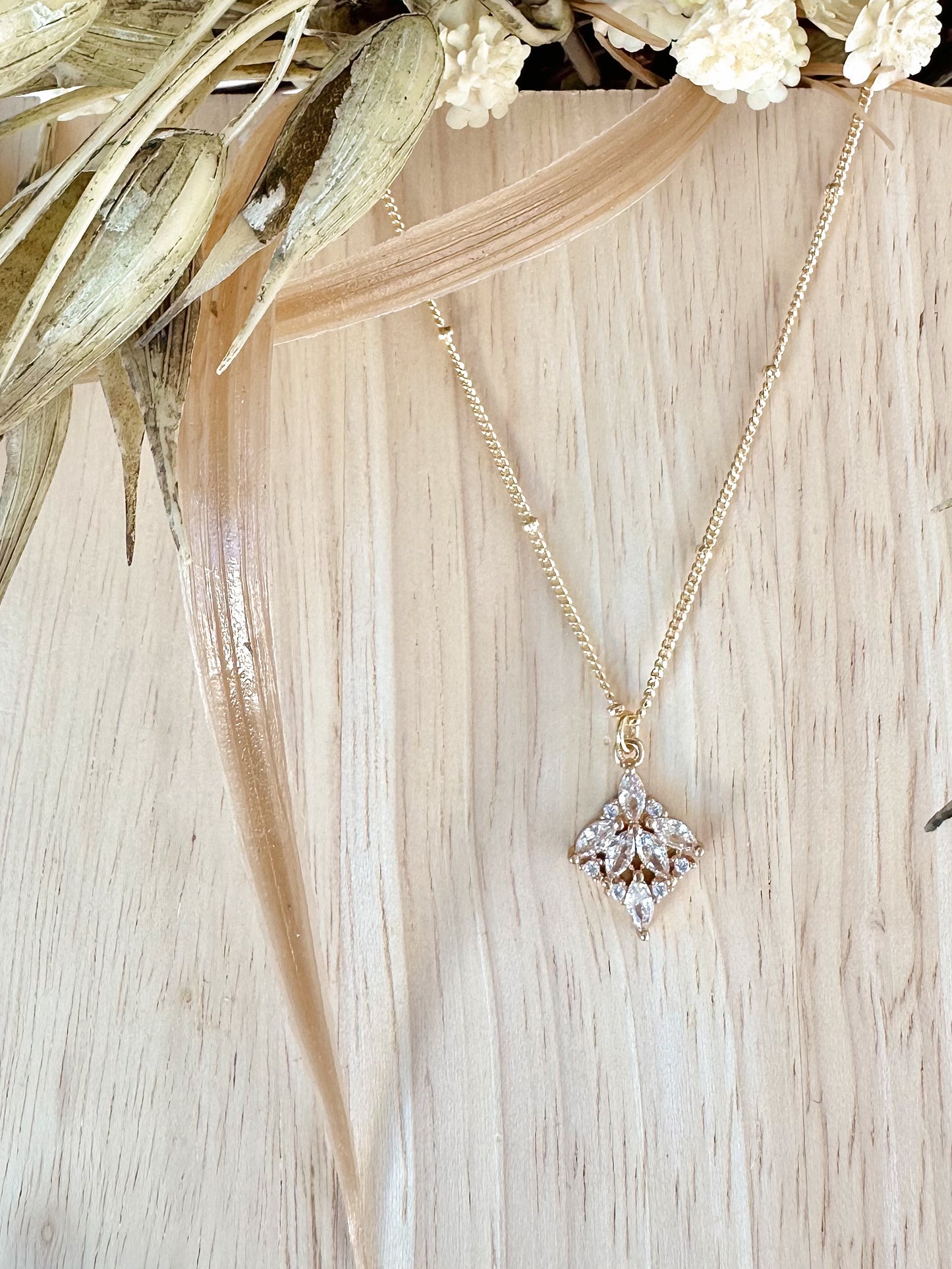 Gold necklace with a cz pendant on a wooden surface with dried leaves and flowers.
