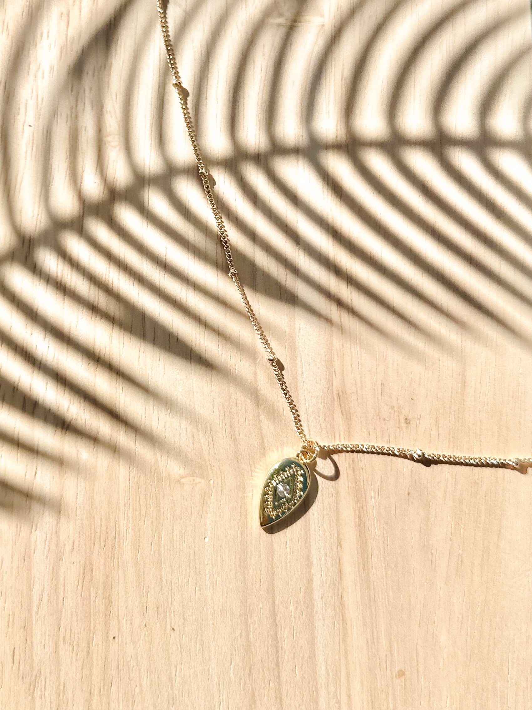 Necklace with a gold pendant on a wooden surface with palm leaf shadow