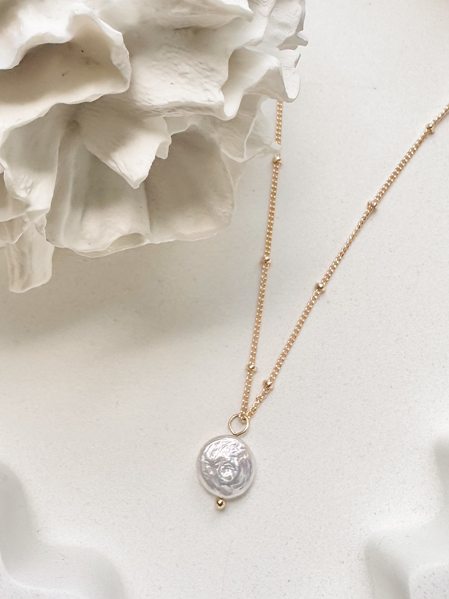 Gold coin pearl necklace displayed against soft white background with coral 