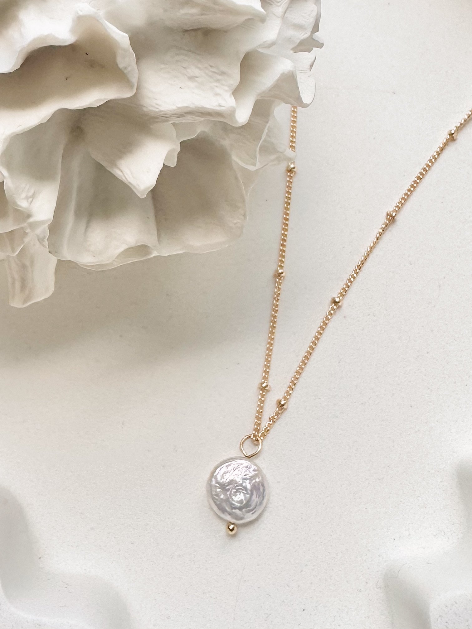 Gold coin pearl necklace displayed against soft white background with coral 