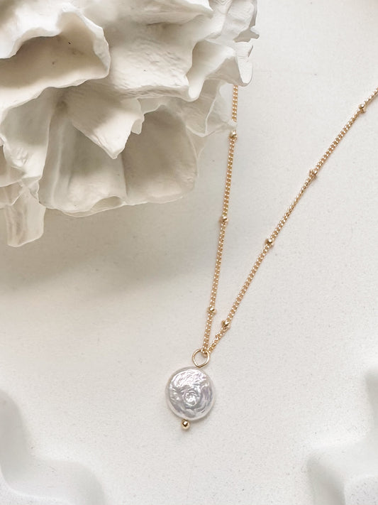 Gold coin pearl necklace displayed against soft white background with coral 