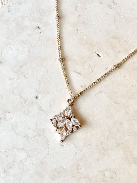 18k gold plated necklace with a marquise cz cluster pendant on a travertine stone background
