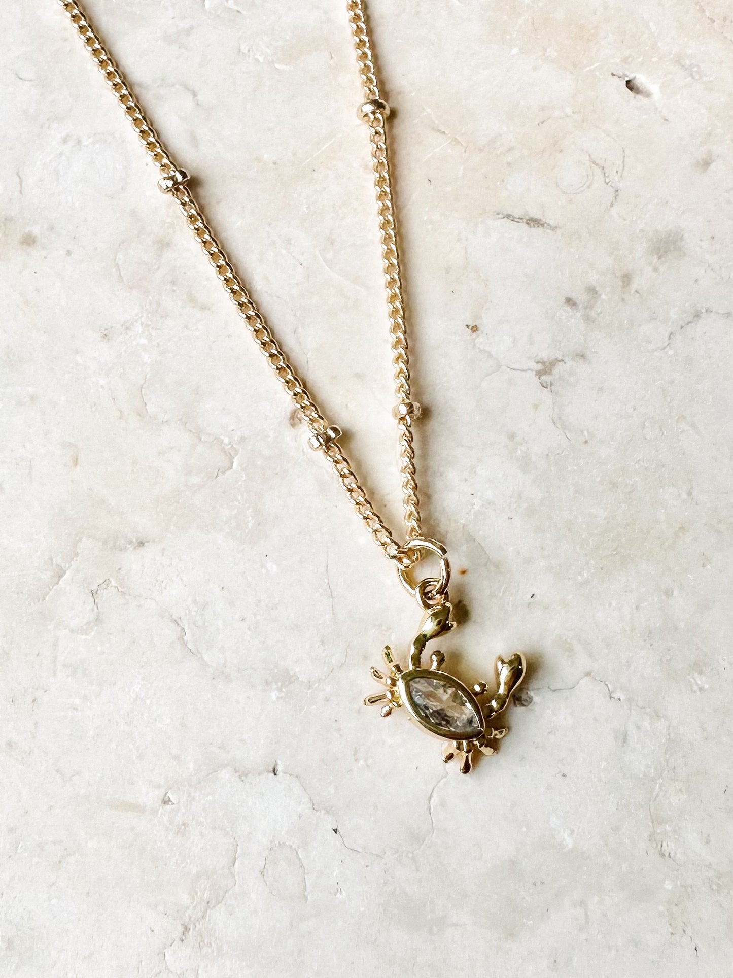 Gold necklace with a small cz crab pendant on a light marble background