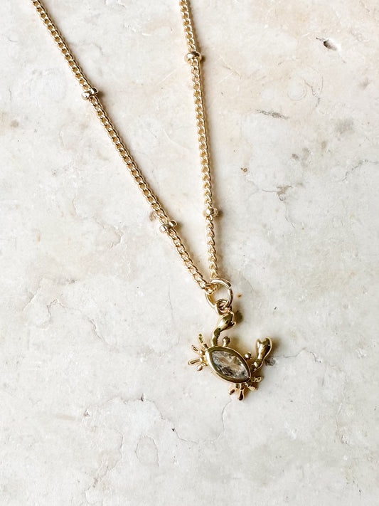 Gold necklace with a small cz crab pendant on a light marble background