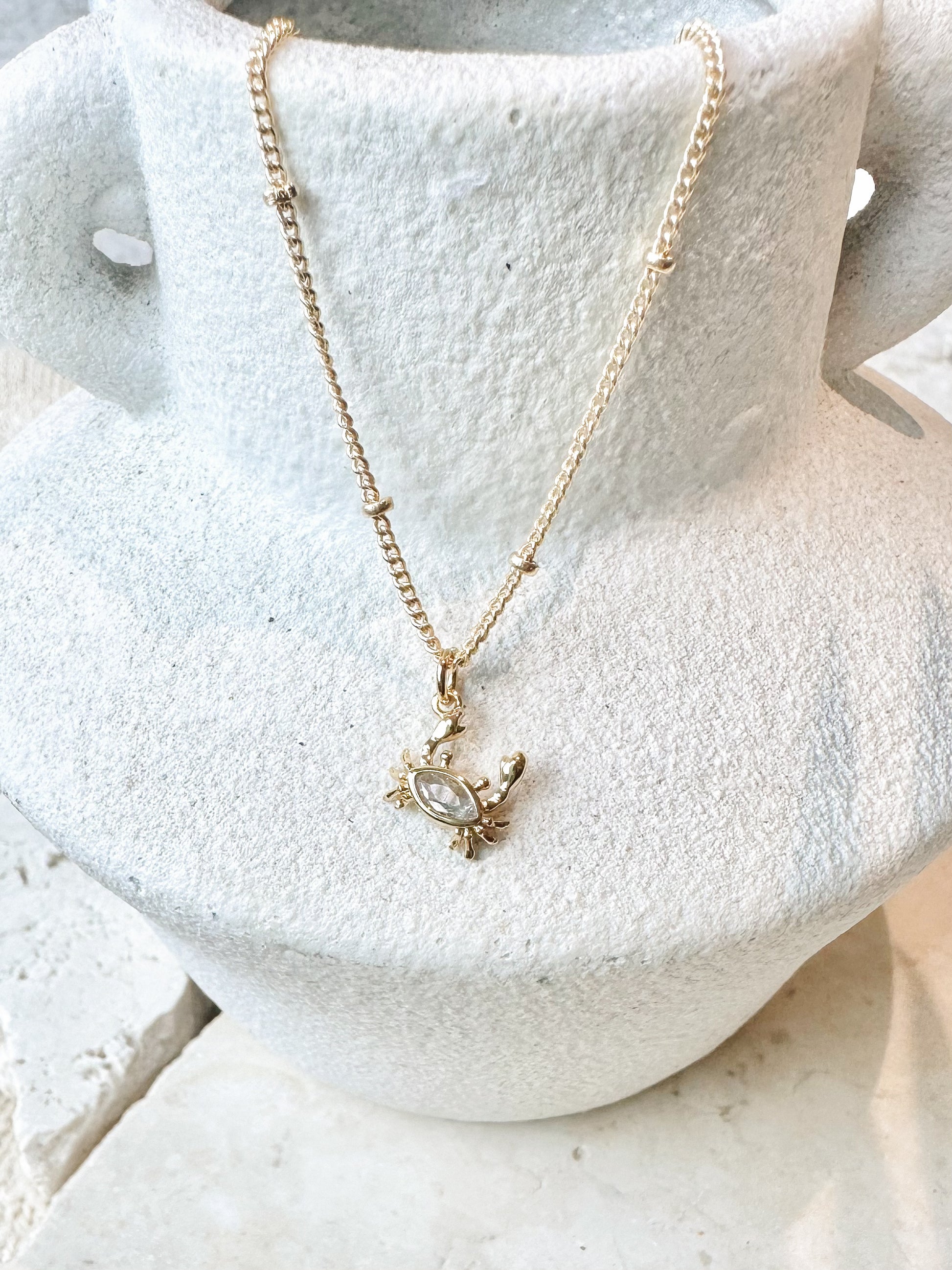 Gold plated stainless steel necklace with a cz crab pendant on a white stone surface