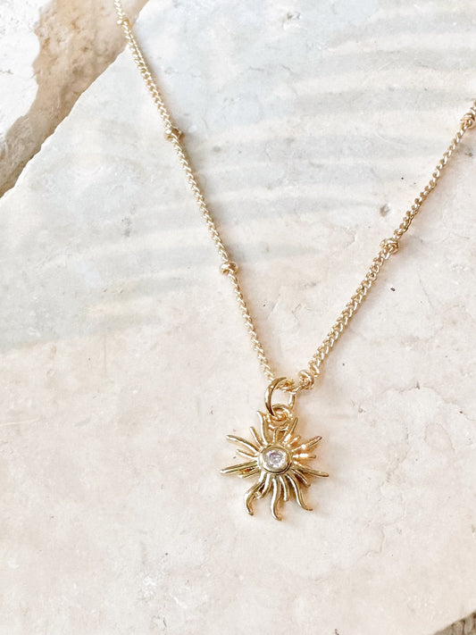Gold necklace with a sun-shaped pendant with a cz centre on a textured travertine stone surface