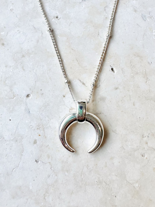 Silver necklace with a crescent moon pendant on a light travertine stone background