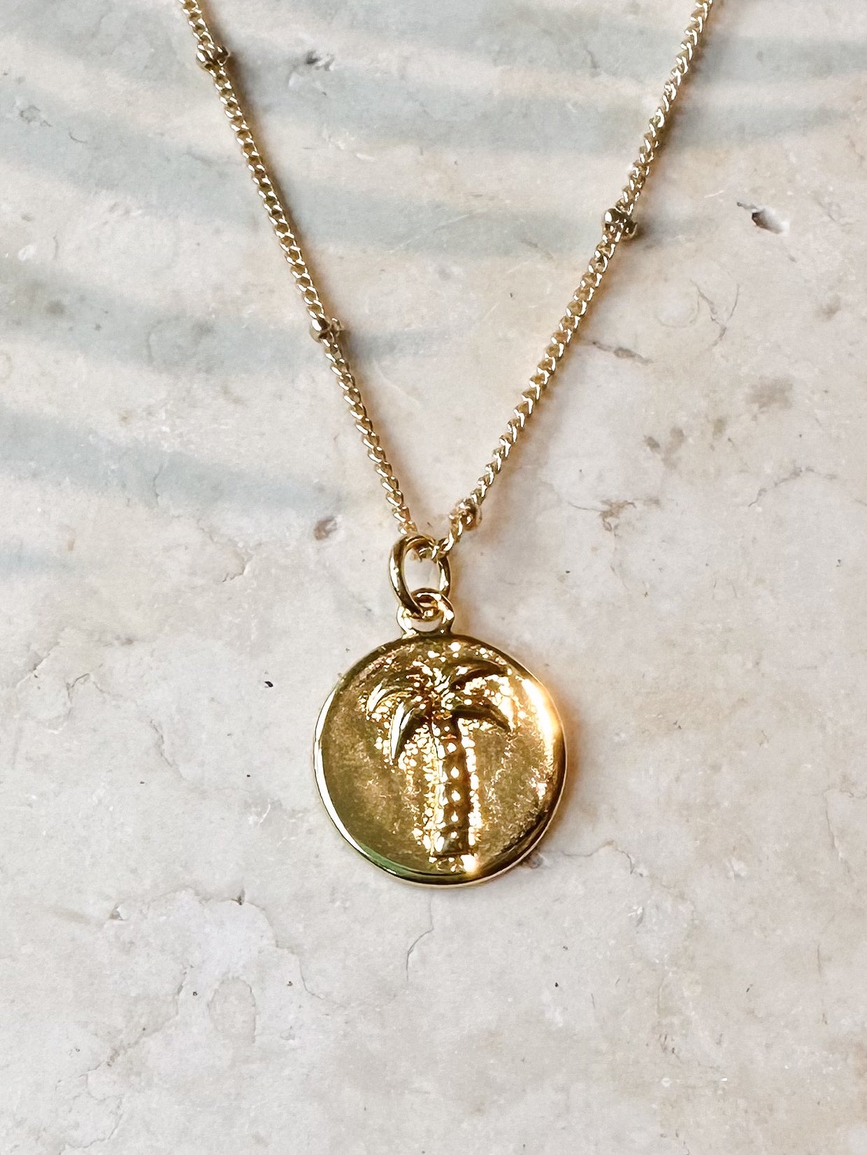 Gold necklace with a palm tree pendant on a light marble background