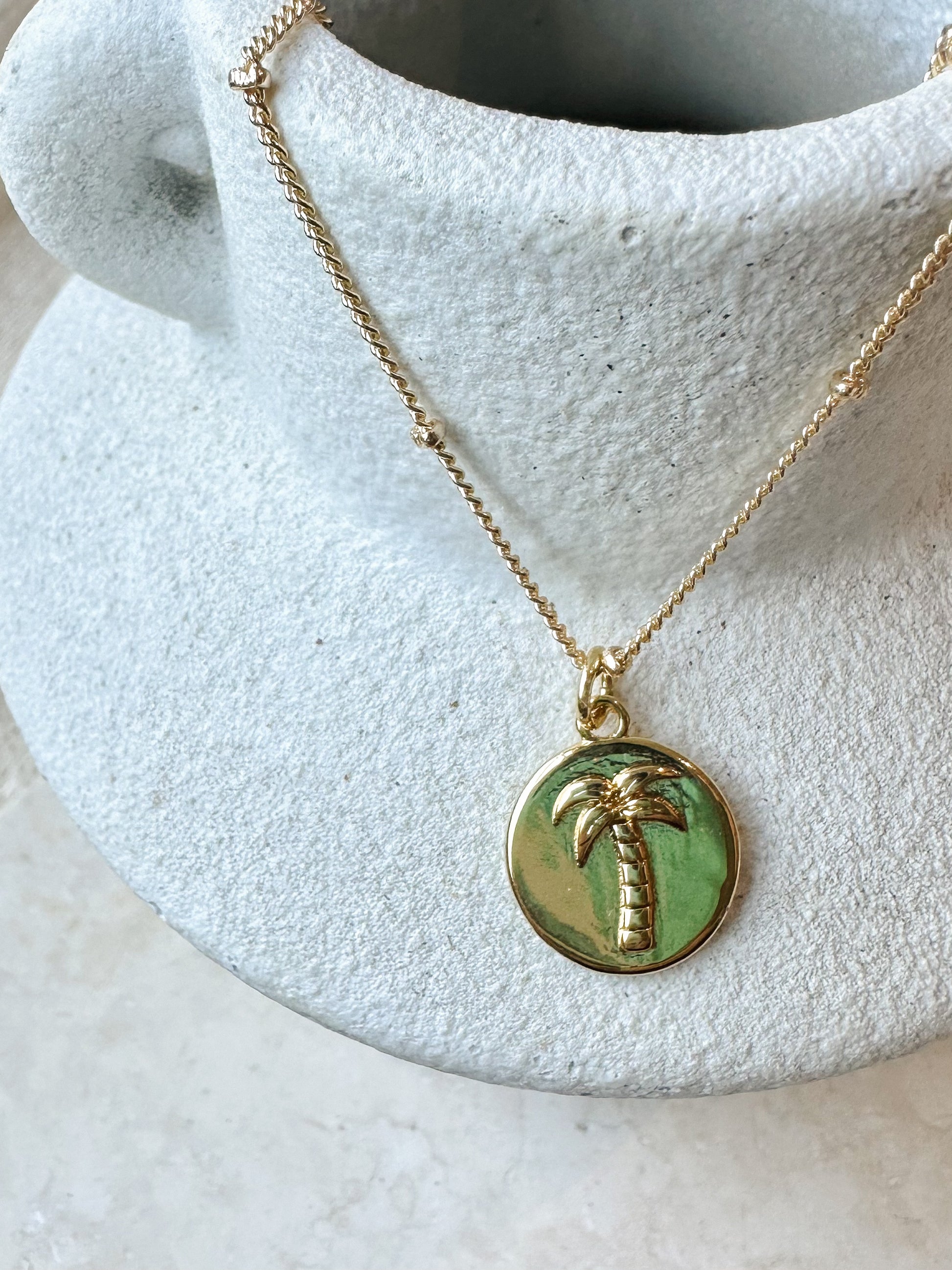 Gold necklace with a palm tree pendant on a textured white surface