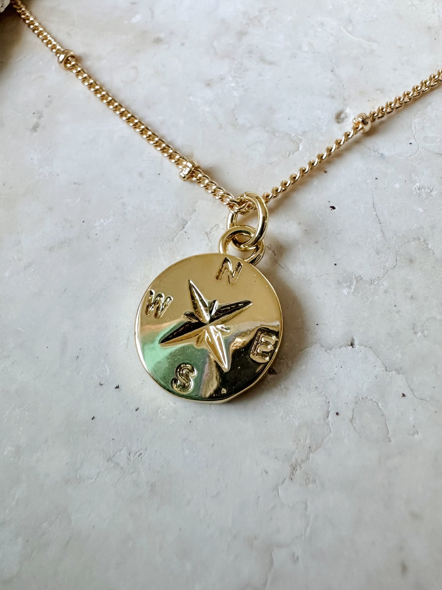 Gold necklace with a compass pendant on a stone surface