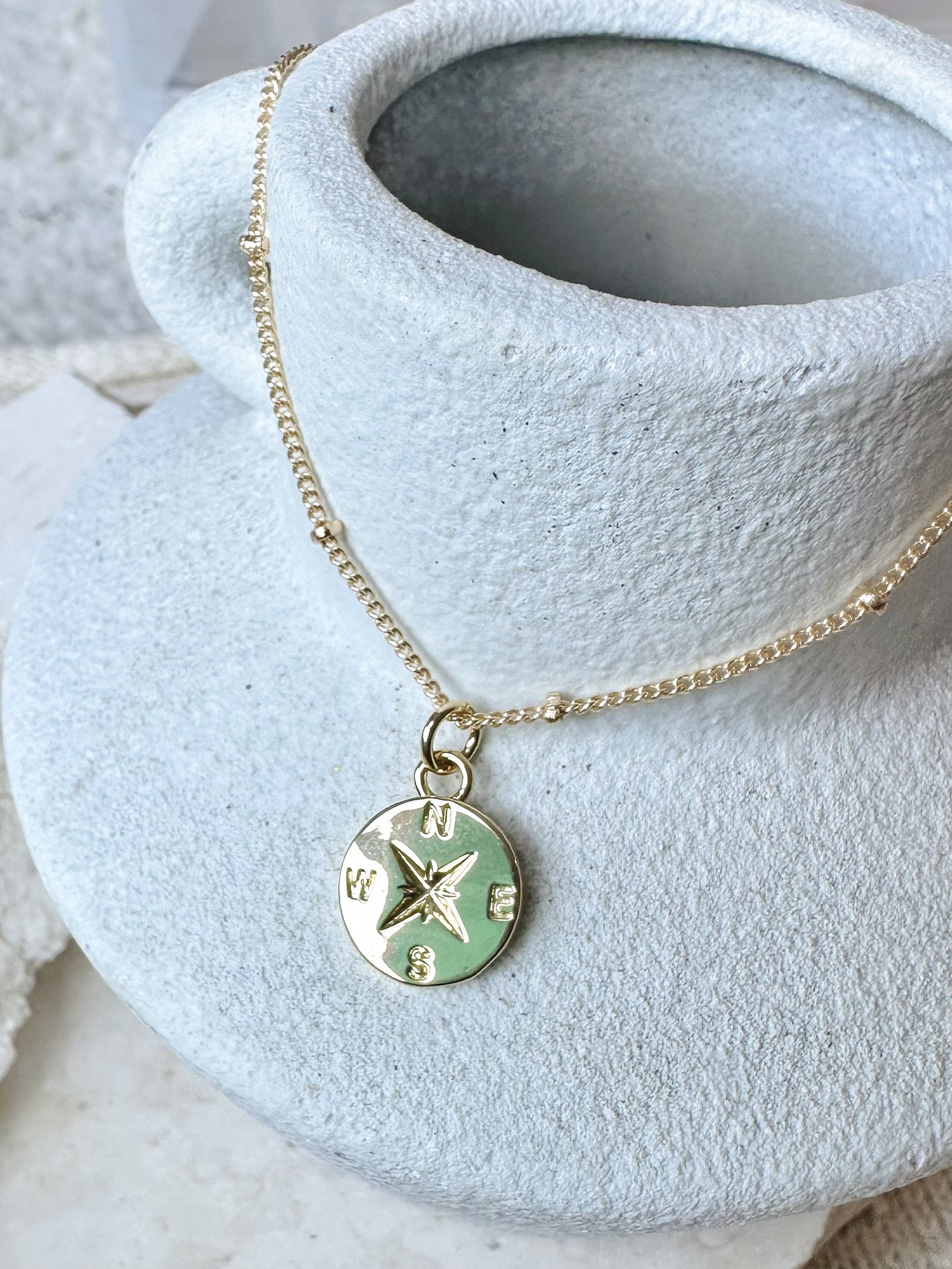 Gold necklace with a compass pendant on a textured stone vase