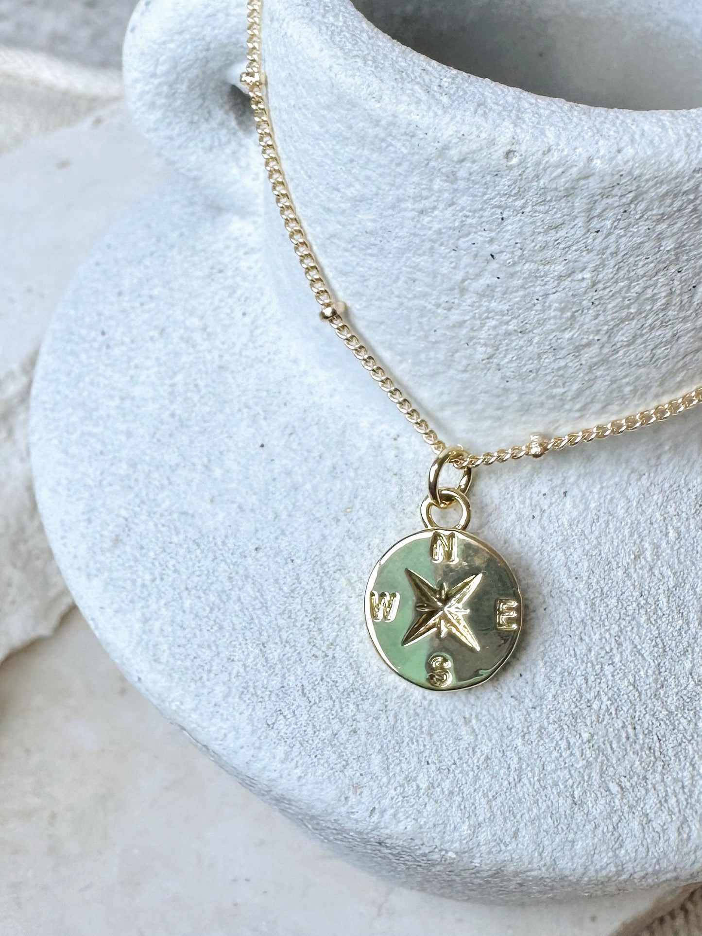 Gold necklace with a compass pendant on a textured stone vase