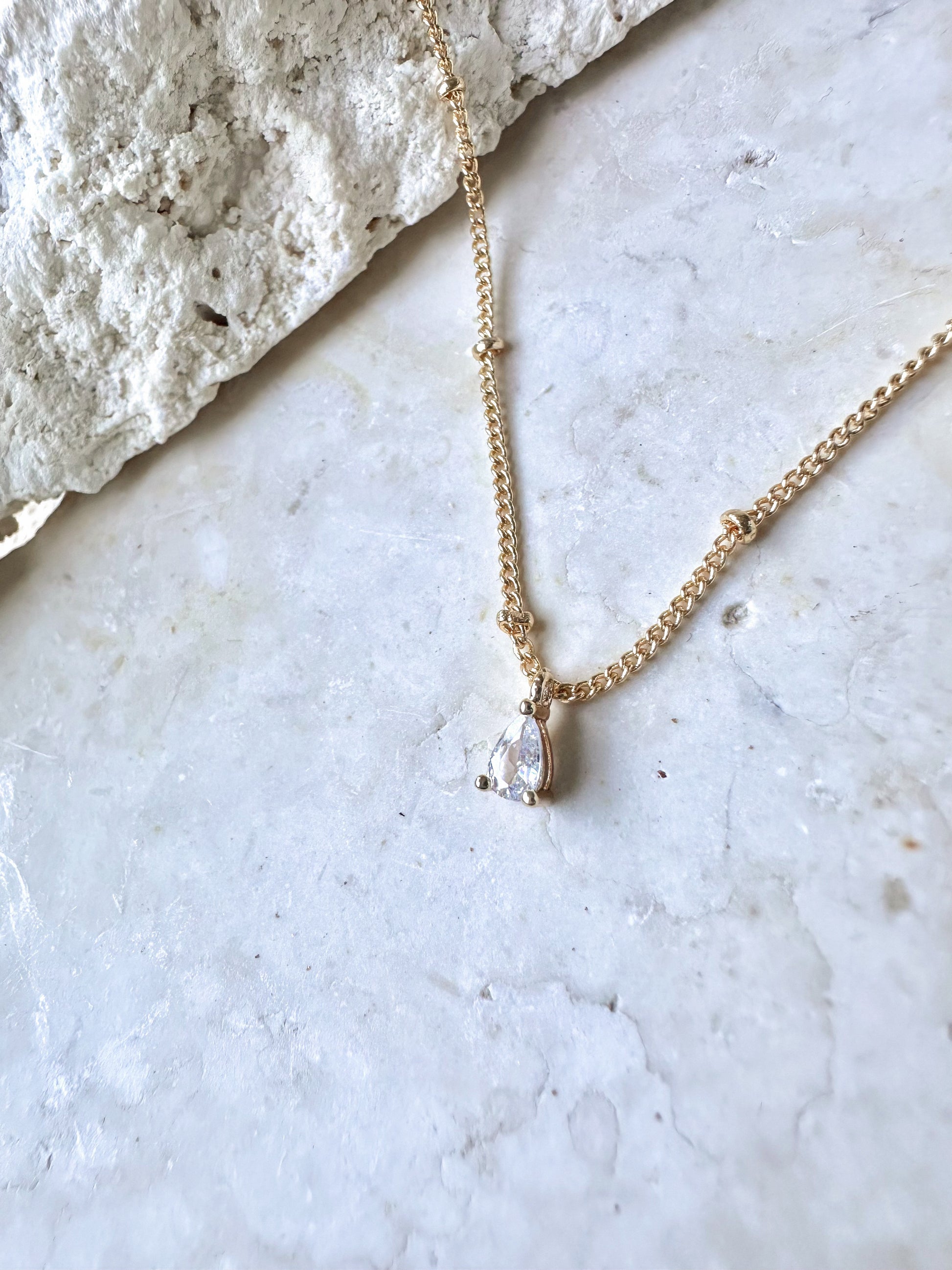 Gold necklace with a cz pear pendant on a travertine stone surface