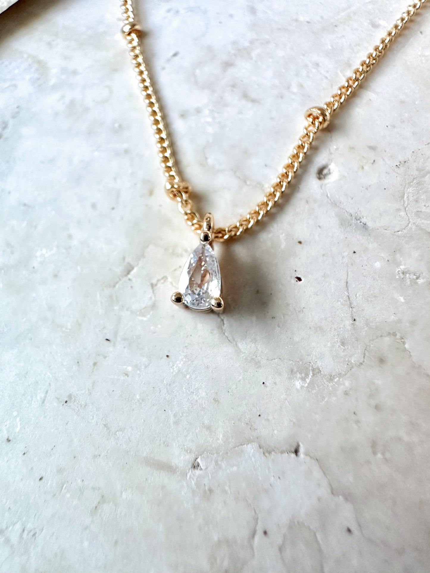 Gold necklace with a teardrop-shaped cz pendant on a marble surface