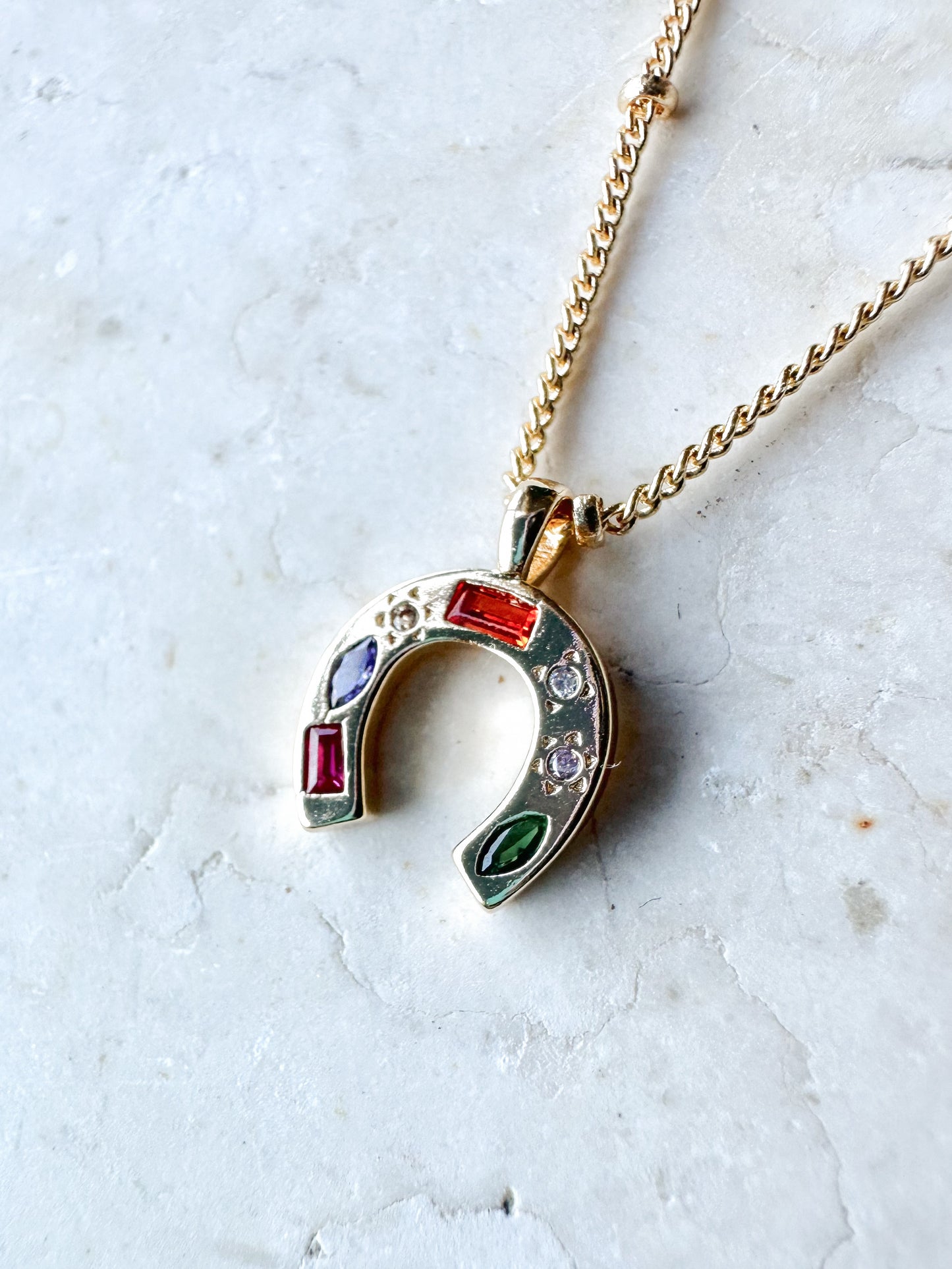Necklace with a colourful cz horseshoe pendant on a light stone background