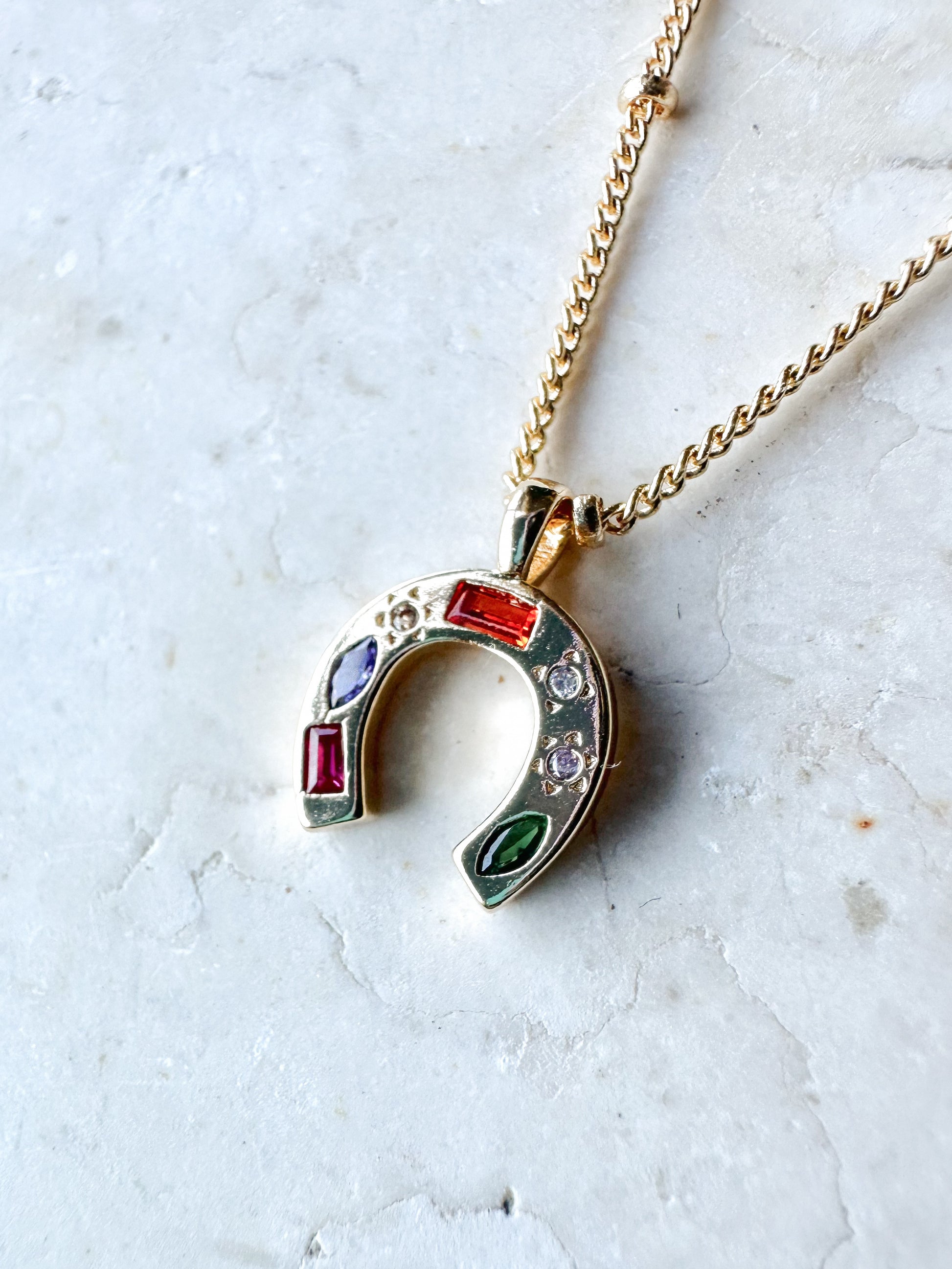 Necklace with a colourful cz horseshoe pendant on a light stone background