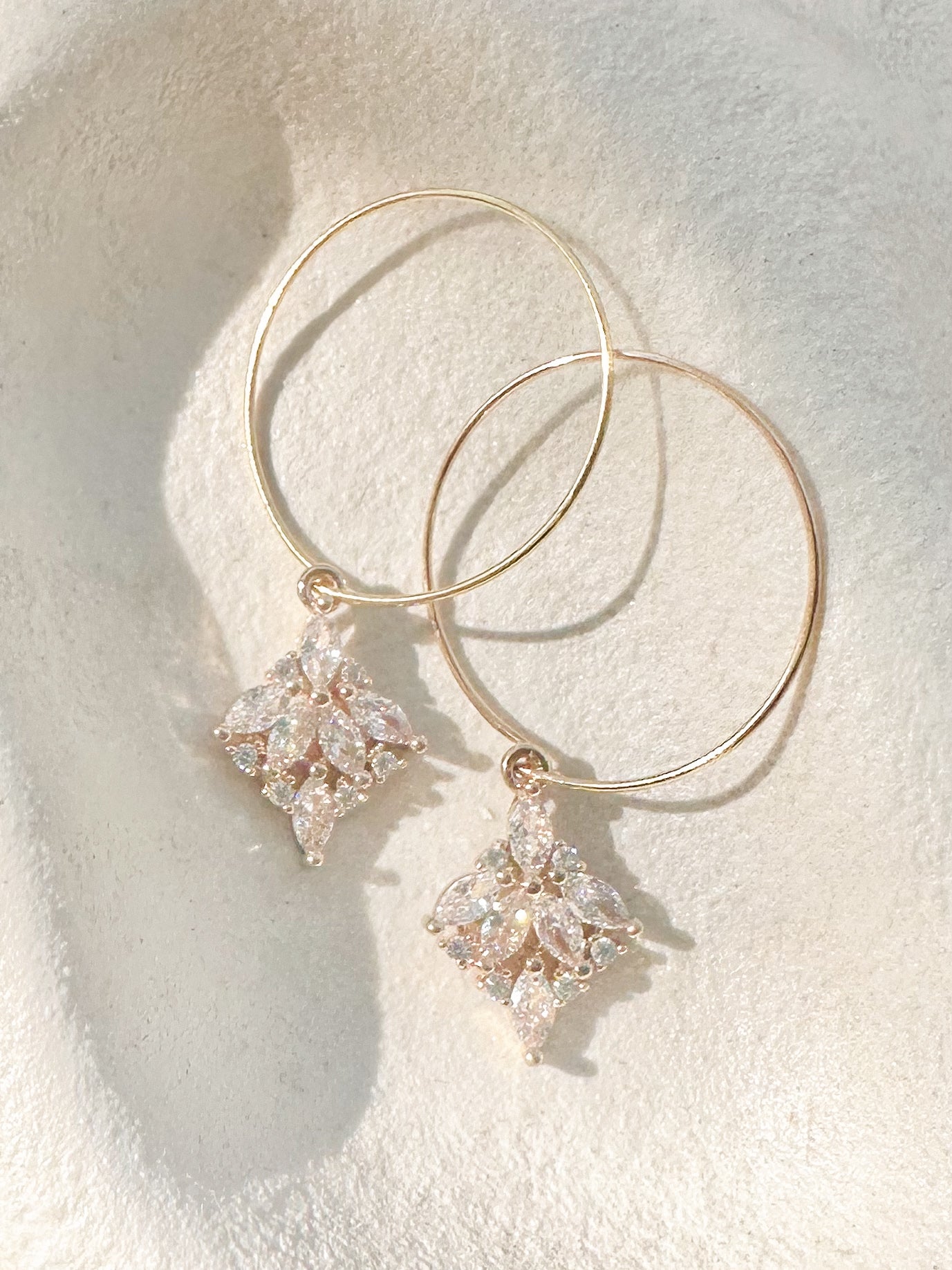 Gold hoop earrings with marquise crystal cluster drops on textured dish.