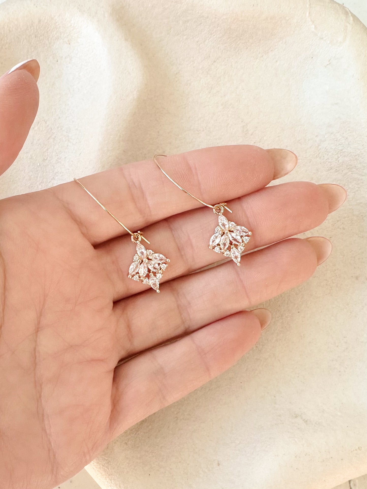 Gold hoop earrings with marquise crystal cluster drops held in hand on textured dish 