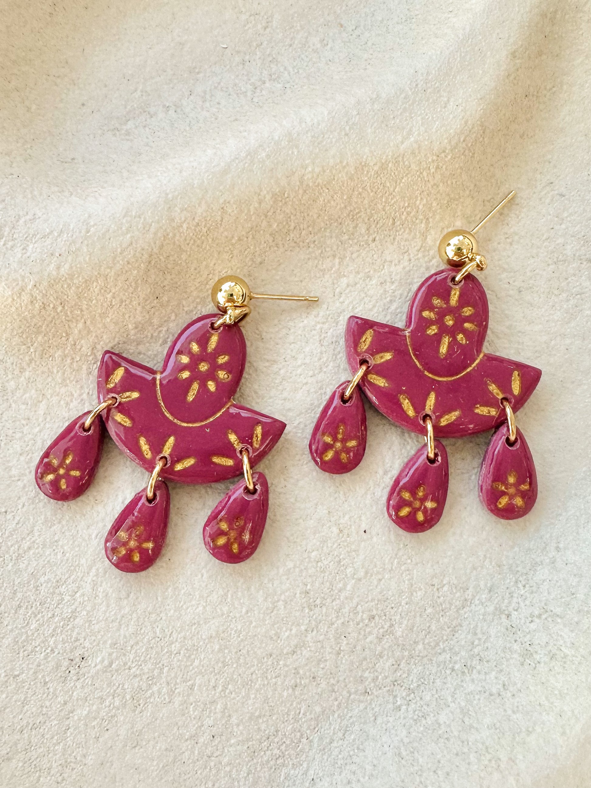 Pair of cherry coloured maroon earrings with gold accents on a stone background