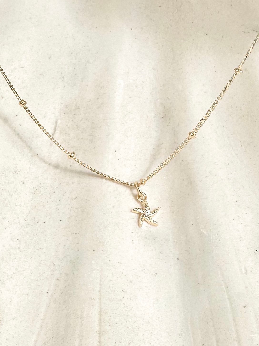 Gold starfish necklace with cubic zirconia centre displayed on sunlit shell background 