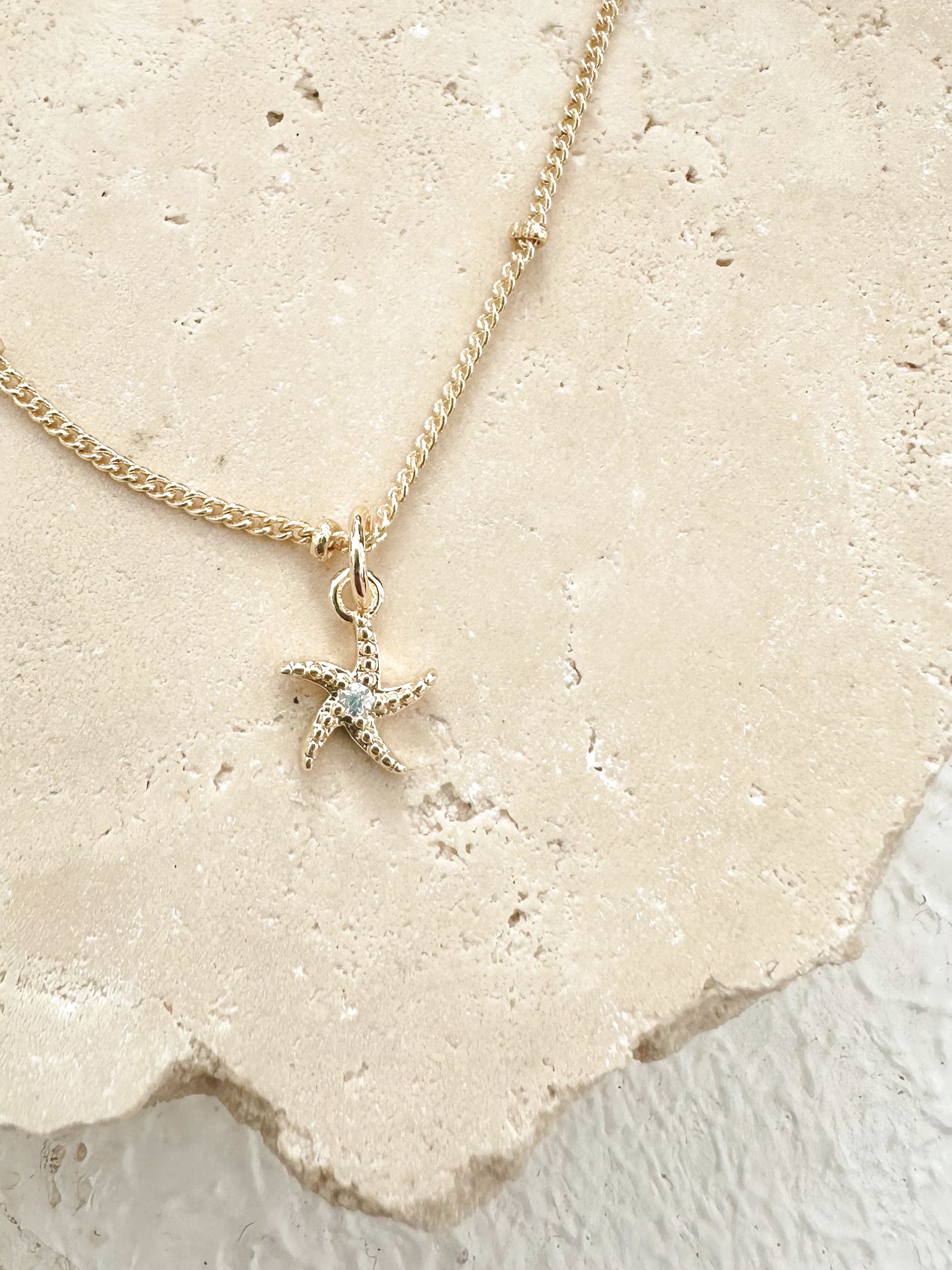 Gold starfish necklace with cubic zirconia centre displayed on textured travertine.