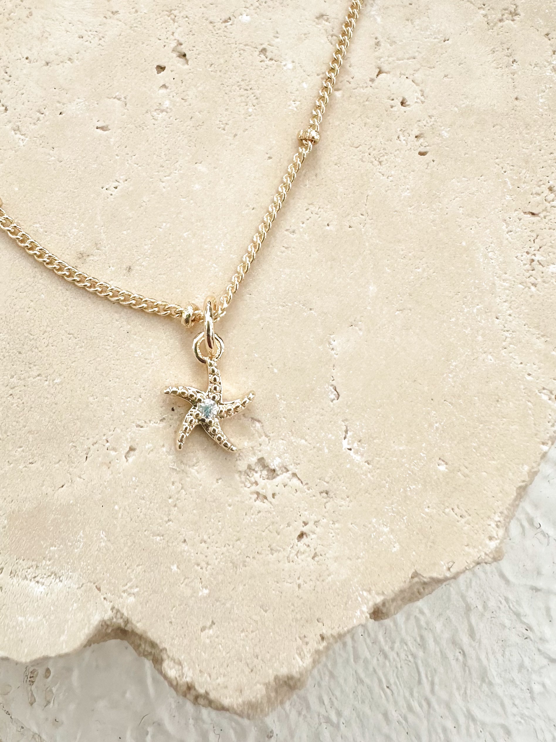 Gold starfish necklace with cubic zirconia centre displayed on textured travertine.