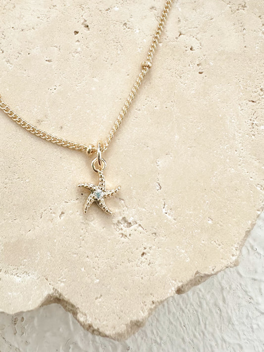 Gold starfish necklace with cubic zirconia centre displayed on textured travertine.