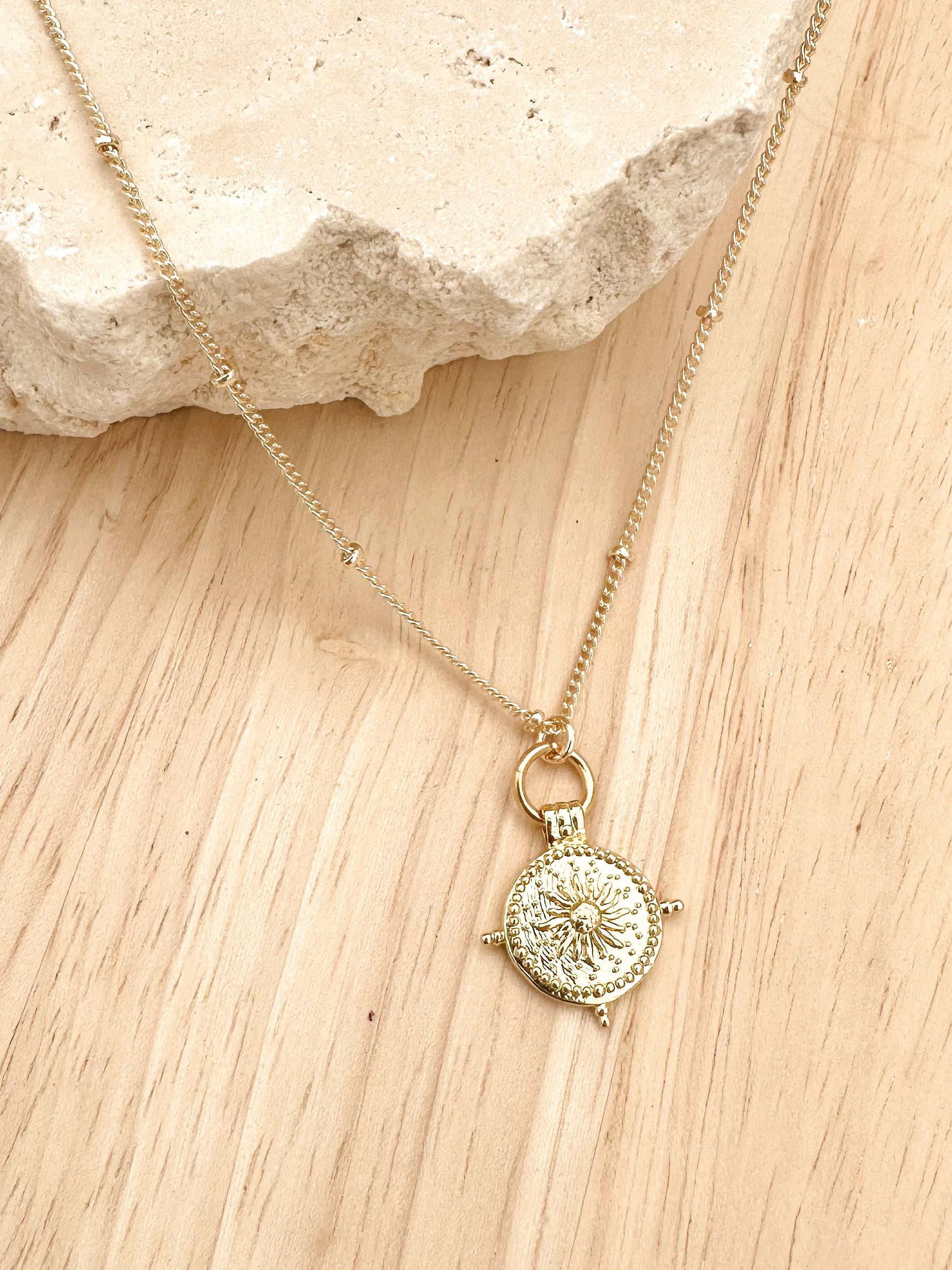 Gold necklace with a circular pendant on a wooden surface