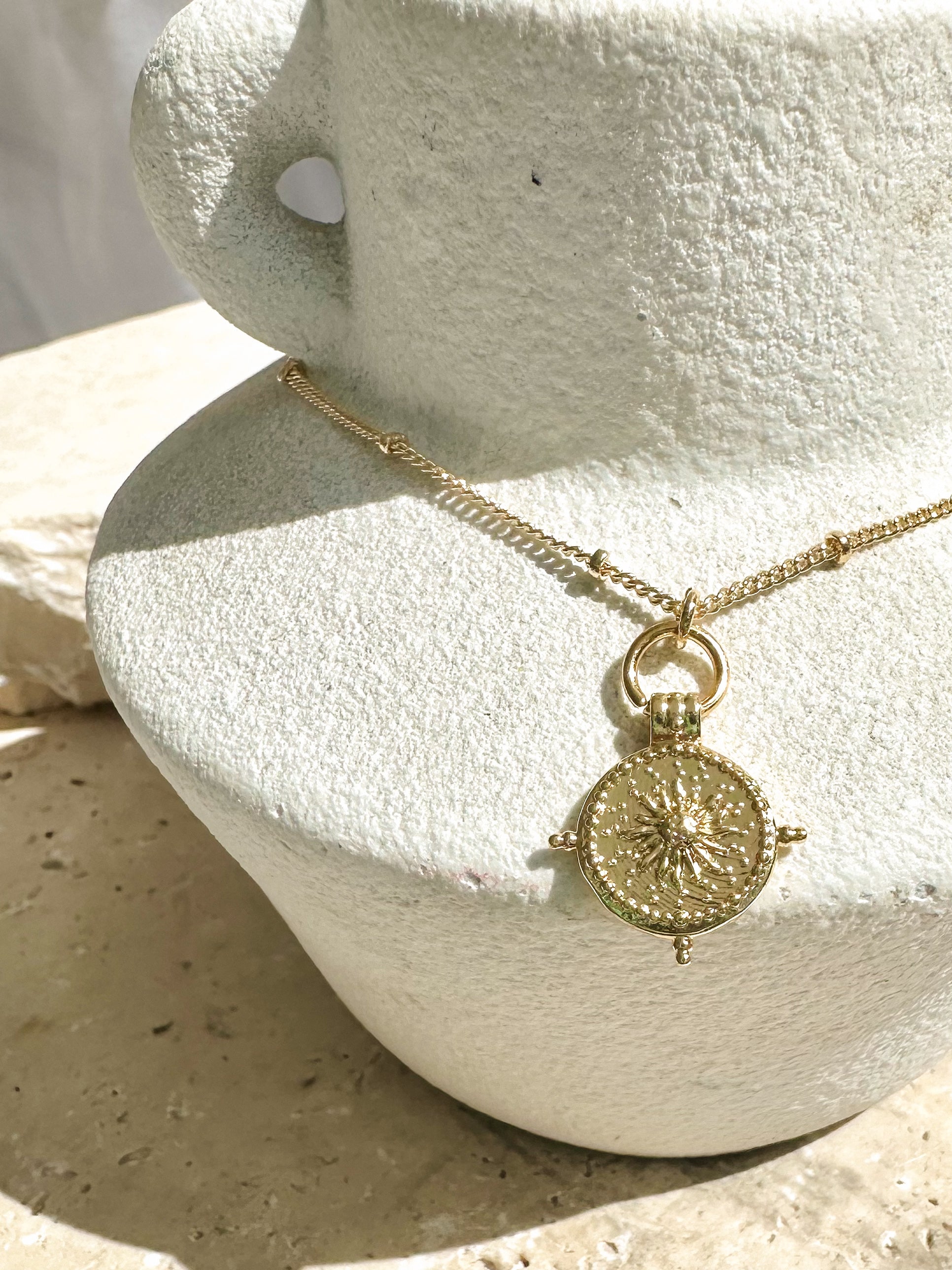 Gold necklace with a detailed pendant on a textured stone surface