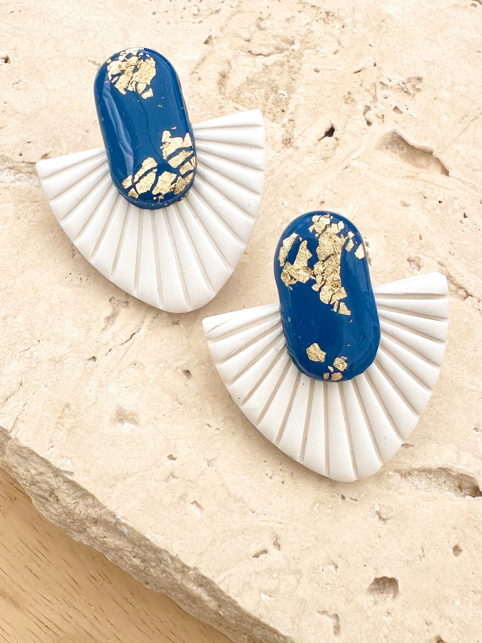 Fan shaped navy and white earrings with gold flake, on a stone surface 