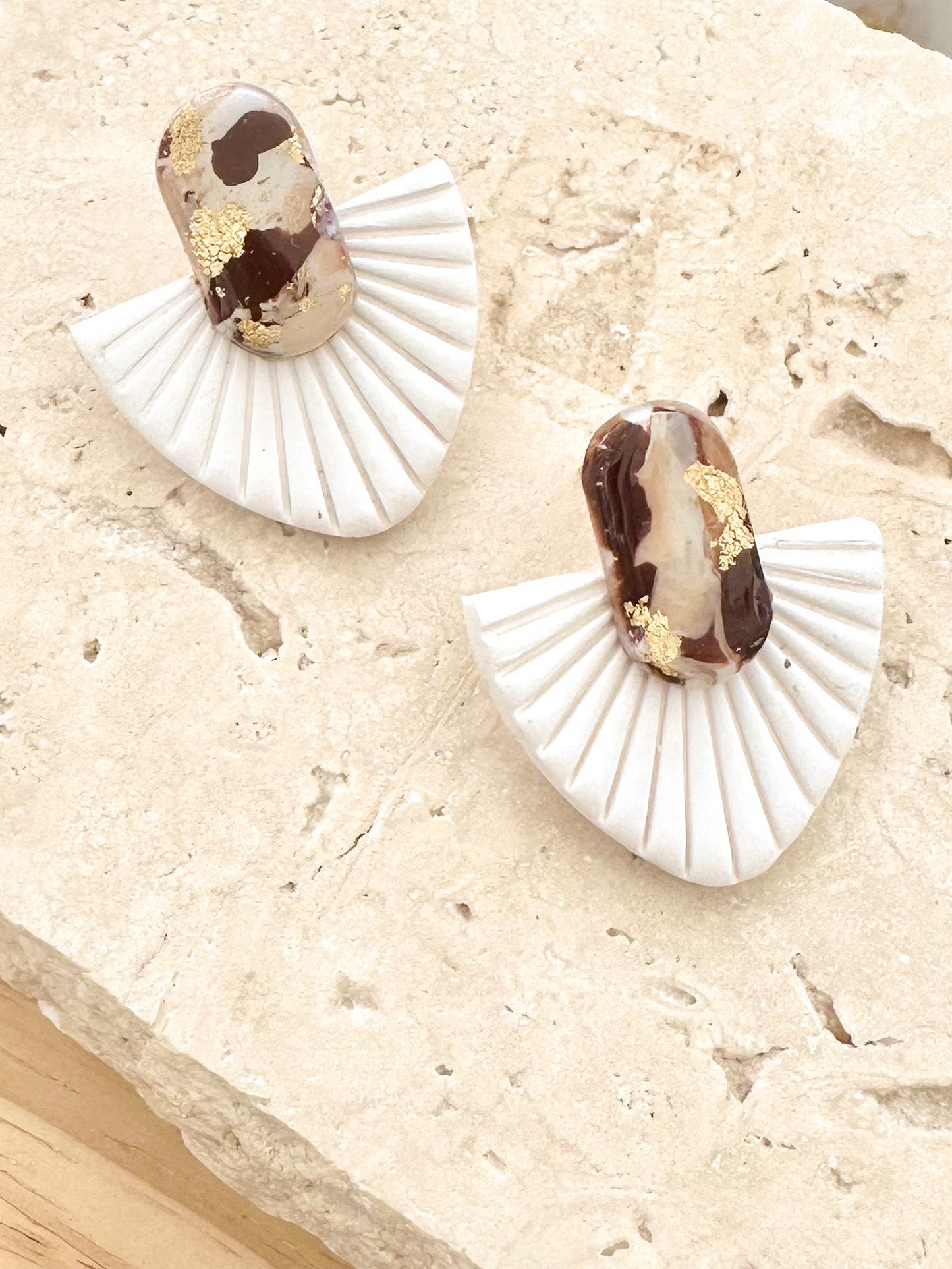 Pair of white fan-shaped earrings with brown and gold accents on a beige surface.