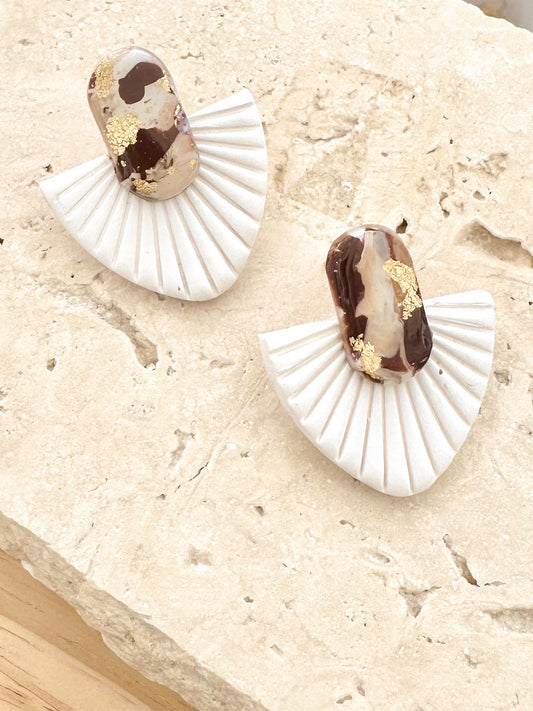 Pair of white fan-shaped earrings with brown and gold accents on a beige surface.